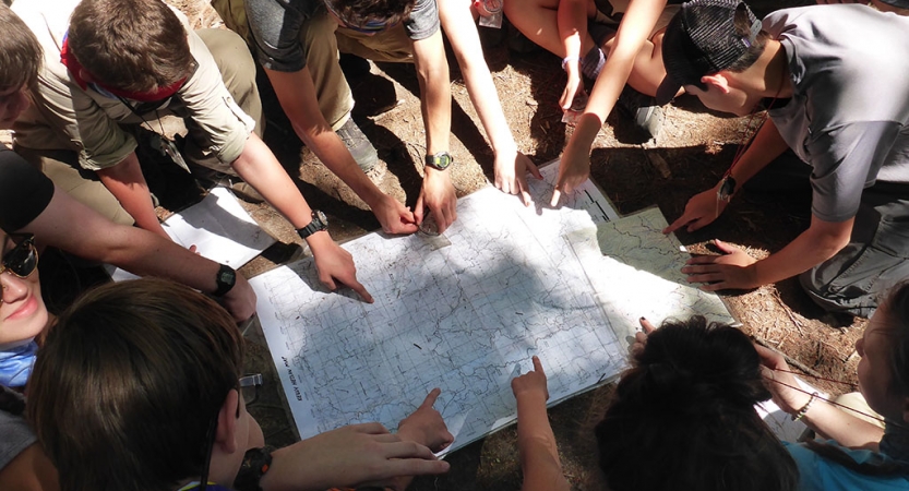 A group of students point at a map laying on the ground.